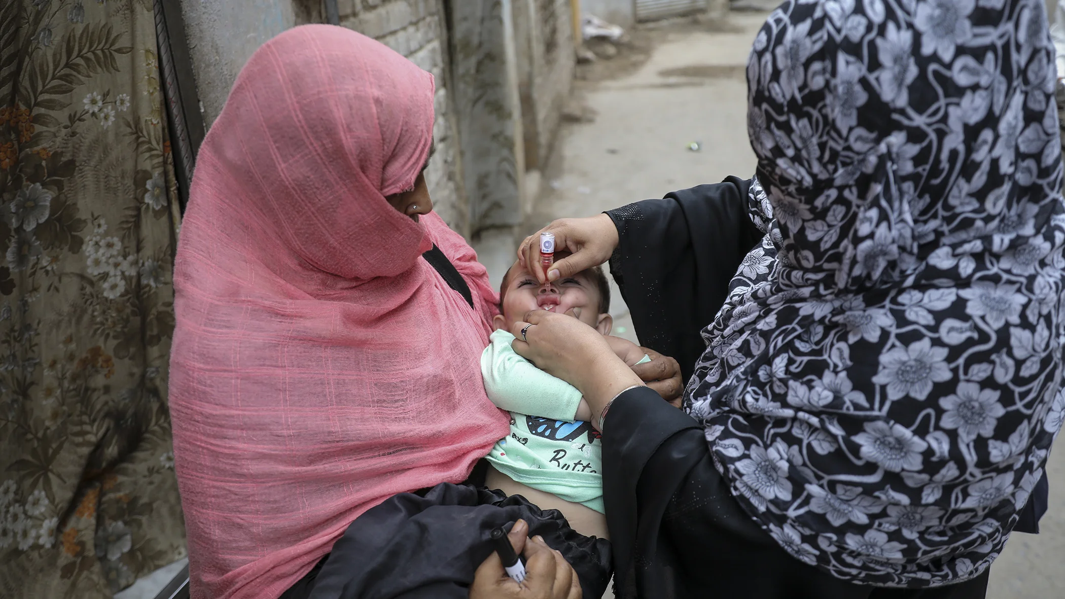 Foto: Pakistan – Aliya Raheem, Gebietsleiterin des Polio-Teams, impft ein kleines Kind während der Tür-zu-Tür-Polio-Kampagne in Rasheed Garhi, Stadt Peshawar, Provinz Khyber-Pakhtunkhwa, Pakistan, gegen Polio.